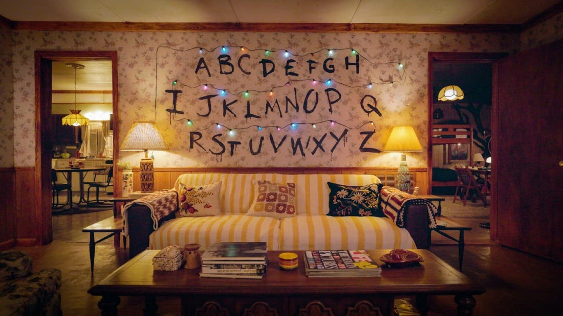The living room of a Hawkins house: alphabet wall, lit string lights and a yellow 80s couch