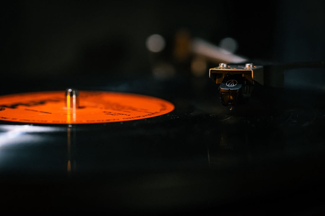 A record spins on the turntable, tonearm down in the groove, orange glints in the half-light