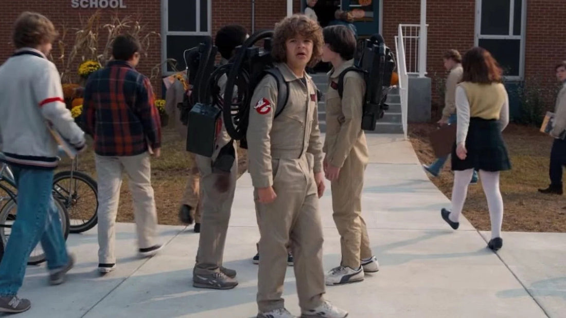 Three teenagers in beige jumpsuits, tanks on their backs, in front of a brick school