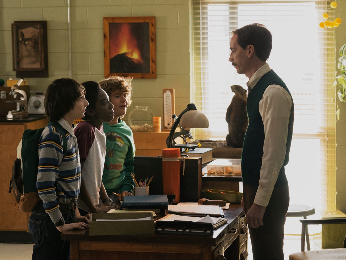 Mr. Clarke, in a green vest, facing Mike, Lucas and Dustin in the science room.